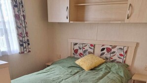 A bedroom with a bed, a headboard with a leaf pattern, and a window with curtains. - Robin hood rhyl, over the road from the beach (Rhyl)