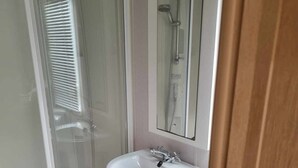 A bathroom with a glass shower enclosure, a white sink, and a mirror. - Robin hood rhyl, over the road from the beach (Rhyl)