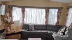 A cozy living room with a grey sofa, a flat-screen TV mounted on the wall, and a wooden cabinet with a TV stand. - Robin hood rhyl, over the road from the beach (Rhyl)