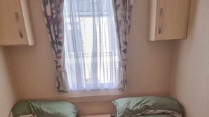 A small room with two beds, a window with sheer curtains, and wooden cabinets. - Robin hood rhyl, over the road from the beach (Rhyl)