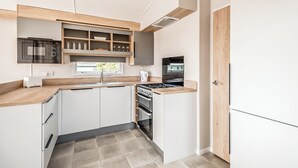 Una cocina compacta con muebles blancos, horno integrado, microondas y estufa.