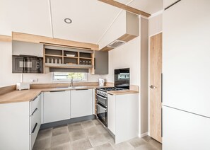 A compact kitchen with white cabinetry, a built-in oven, a microwave, and a stove. - 2 bedroom accommodation in Castle Douglas (Castle Douglas)