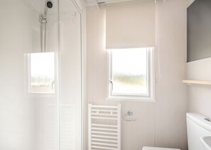 A bathroom with a shower, a toilet, a towel rack, and a window.