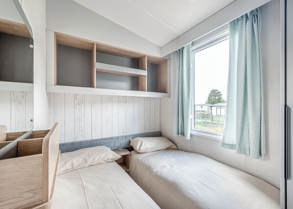 A room with a bunk bed, a desk, and a window with curtains.