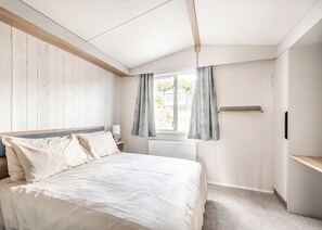 A bedroom with a bed, bedside table, lamp, window with curtains, radiator, and a shelf. - 2 bedroom accommodation in Castle Douglas (Castle Douglas)