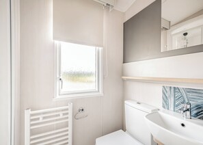 A bathroom with a window, a toilet, a sink, and a mirror with a decorative backsplash. - 2 bedroom accommodation in Castle Douglas (Castle Douglas)