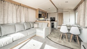 Un espacio moderno para relajarse con sofá, una mesa de comedor con sillas, cocina equipada y vistas al exterior.