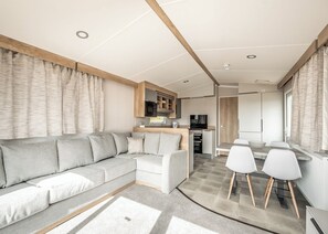 A modern living area with a sofa, a dining table with chairs, a kitchen with appliances, and a view of the outdoors. - 2 bedroom accommodation in Castle Douglas (Castle Douglas)