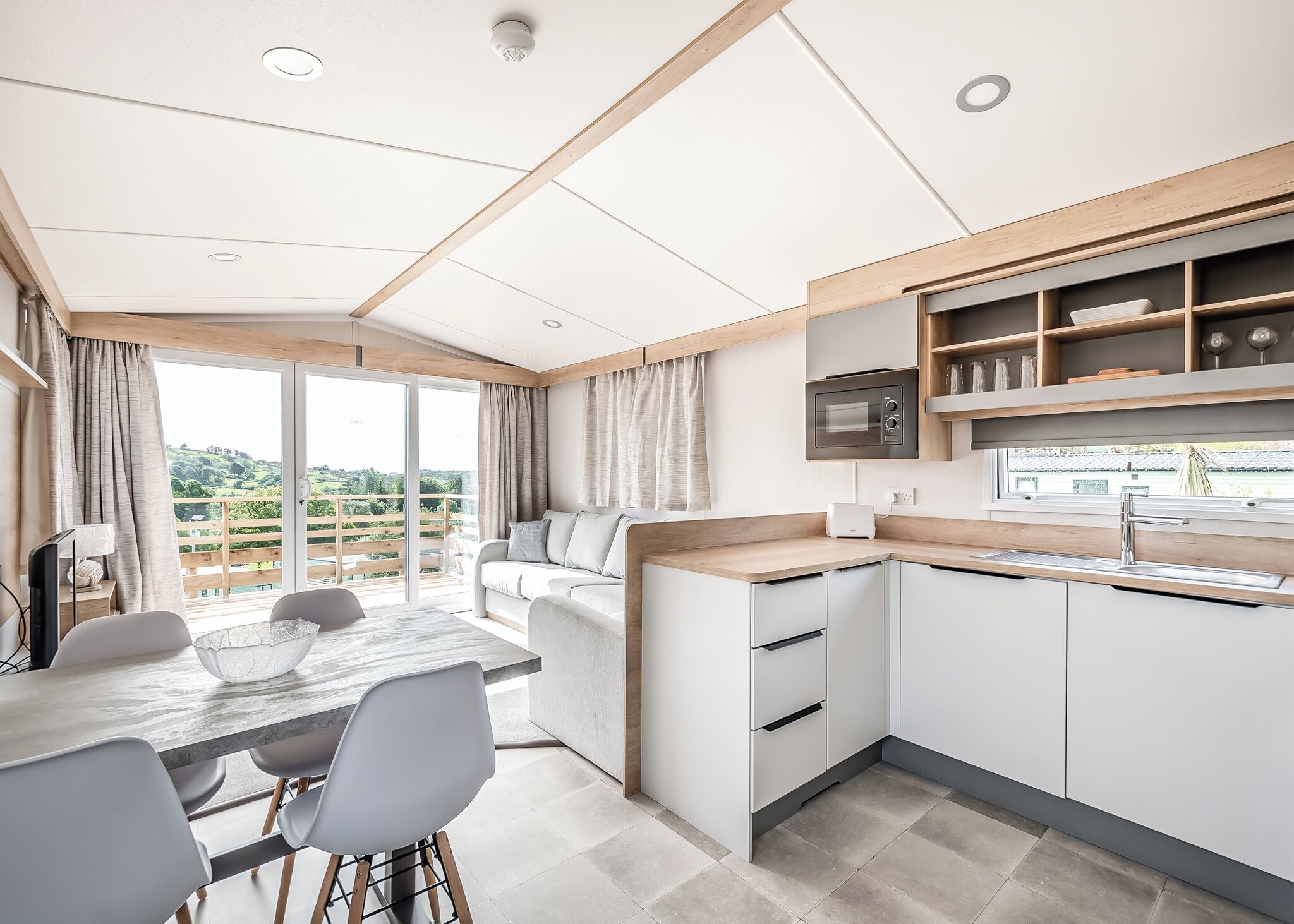 Uma cozinha moderna com micro-ondas embutido, um espaço de refeições com mesa e cadeiras, e vista para o verde através da porta de correr de vidro.