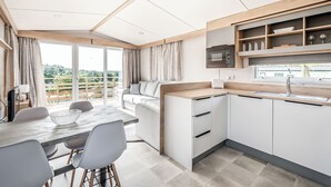 Une cuisine moderne dotée d’un four à micro-ondes encastré, d’un coin repas avec une table et des chaises, et offrant une vue sur la verdure grâce à une porte-fenêtre coulissante.