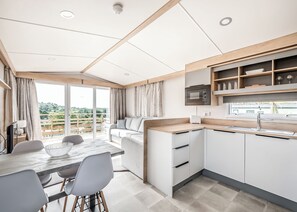 Eine moderne Küche mit integriertem Mikrowellenherd, einem Essbereich mit Tisch und Stühlen sowie Blick auf Grünflächen durch eine Schiebetür.