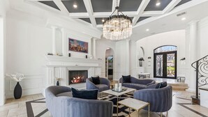 A spacious living room with a fireplace, comfortable seating, and a chandelier. - Mansion at Reunion | 11BR Luxe Stay w/ Private Pool, Theater, Arcade, and Themed Rooms near Disney (Kissimmee)
