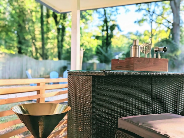 A covered outdoor seating area with a wicker table, a metal bowl, and a wooden box with a metal object on top.