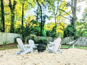 A backyard with a fire pit, four Adirondack chairs, and a wooden fence.