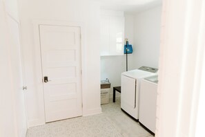 A laundry room with a white door, a washing machine, and a blue laundry basket on the wall.