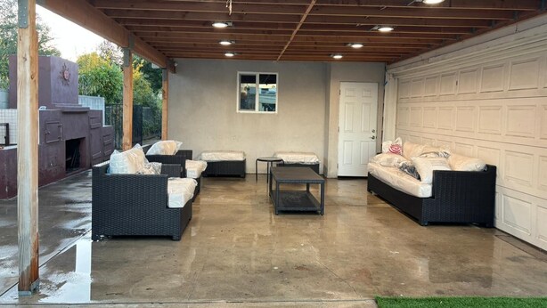 Un patio couvert aménagé avec des meubles en osier, une petite table et une porte donnant sur un garage.