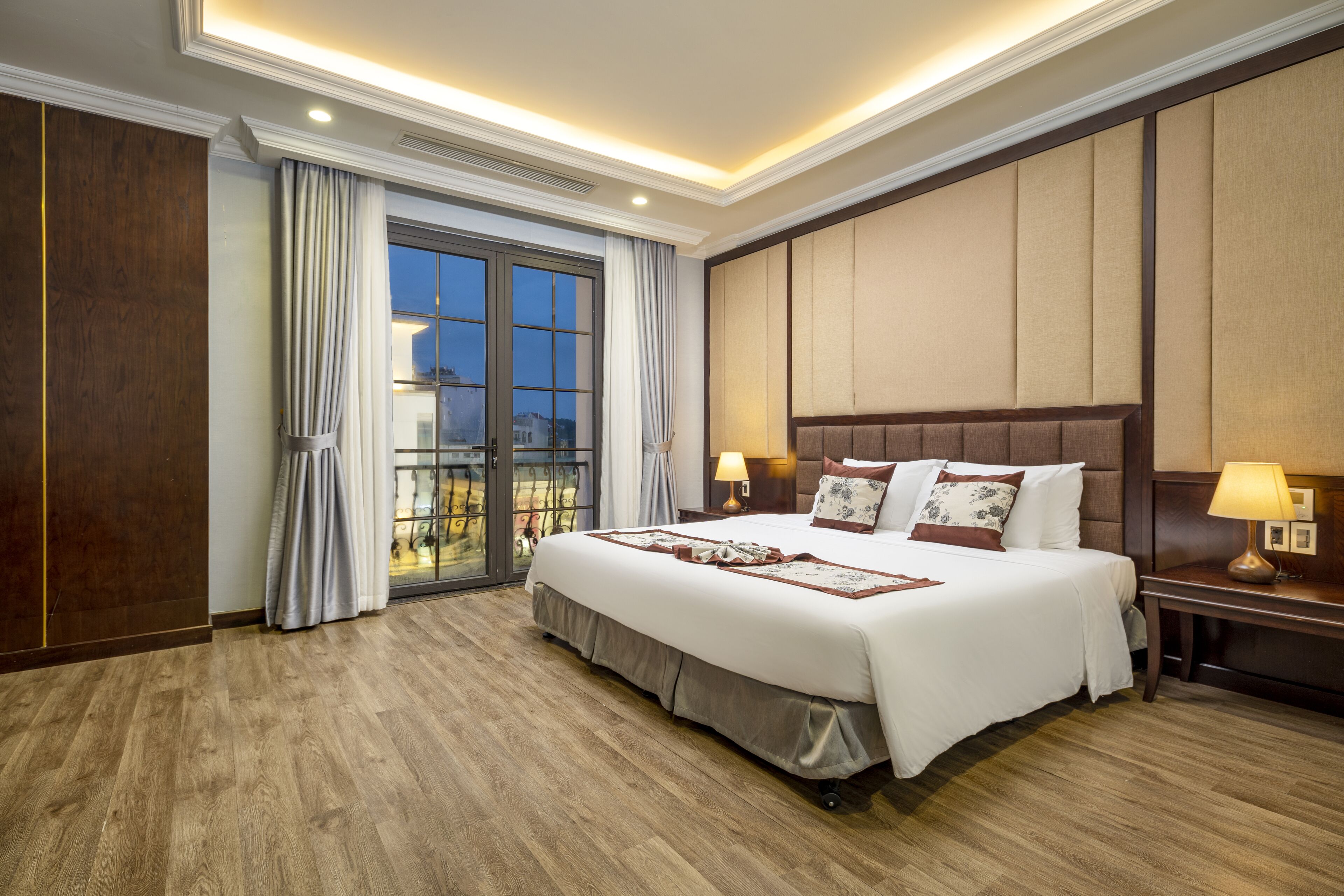 Une chambre d’hôtel avec un grand lit, un plancher en bois, une vue sur l’extérieur grâce à une porte coulissante, et une table de chevet avec une lampe.