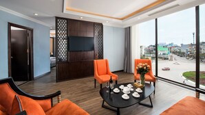 A modern hotel room with a large window, two orange armchairs, a black coffee table, and a TV mounted on the wall. - Móng Cái Place (Mong Cai)