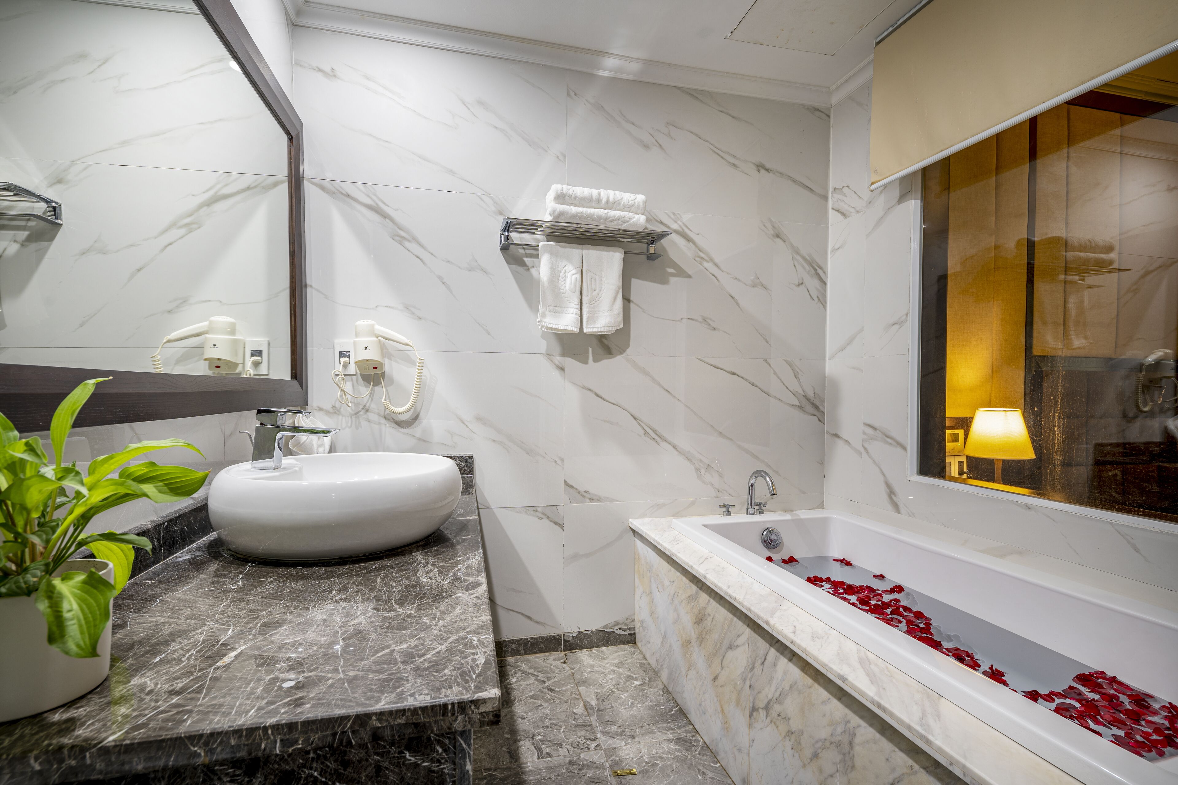 Une salle de bain moderne avec un lavabo en marbre, une baignoire parsemée de pétales de rose et un miroir doté d’un porte-serviettes.