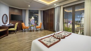 A hotel room with a large bed, two chairs, a desk, a TV, and a balcony with a view of the city. - Móng Cái Place (Mong Cai)