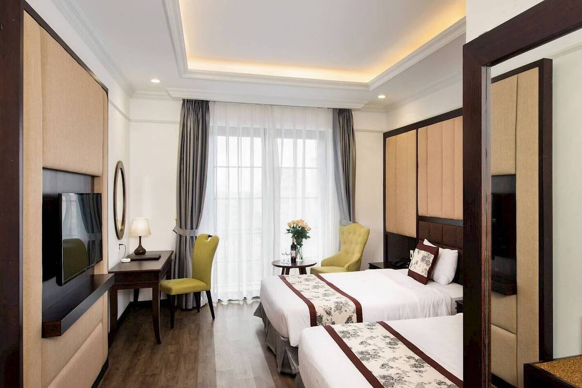 Habitación de hotel con cama, escritorio con televisor, silla y ventana con cortinas.