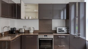 A modern kitchen with dark cabinetry, a built-in oven, a microwave, a coffee maker, and a kettle. - Clean Shoreditch 1BR w/ Open Plan, nr Market & Dining, by Blueground (London)