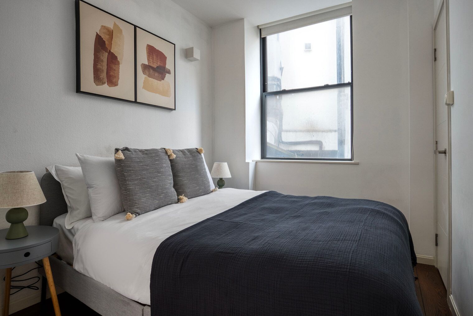A neatly arranged bedroom with a bed, pillows, a bedside table with a lamp, and a window with a view.