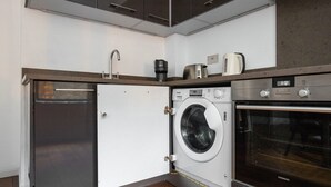 A compact kitchen with a built-in washer and dryer, a coffee maker, and a microwave. - Clean Shoreditch 1BR w/ Open Plan, nr Market & Dining, by Blueground (London)