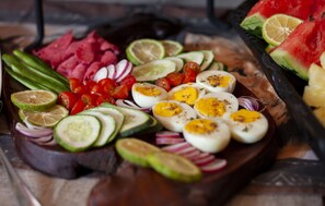 Ein Holzbruch mit Gurkenscheiben, Tomaten, Zwiebeln und gekochten Eiern, verziert mit Limettenscheiben und Kräutern.