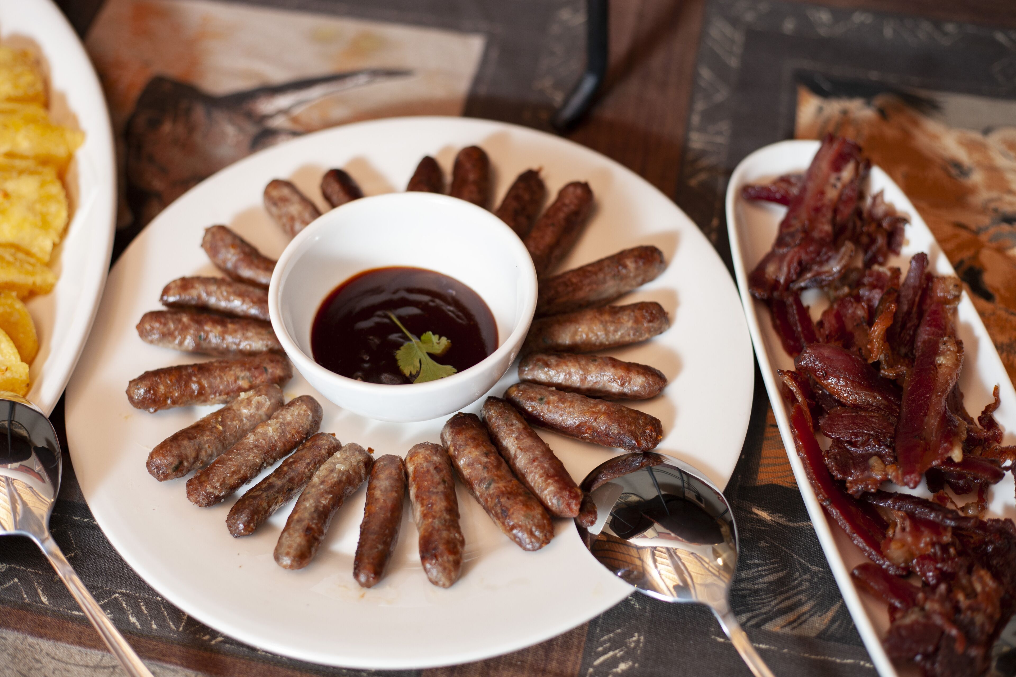 A plate of sausages arranged in a circle with a bowl of sauce in the center.