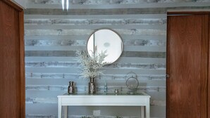 Une pièce avec un mur recouvert de lambris en bois, un miroir rond et une console blanche agrémentée d’objets décoratifs.