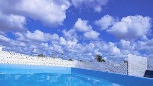 Une piscine entourée d’une clôture blanche, avec des palmiers en arrière-plan.