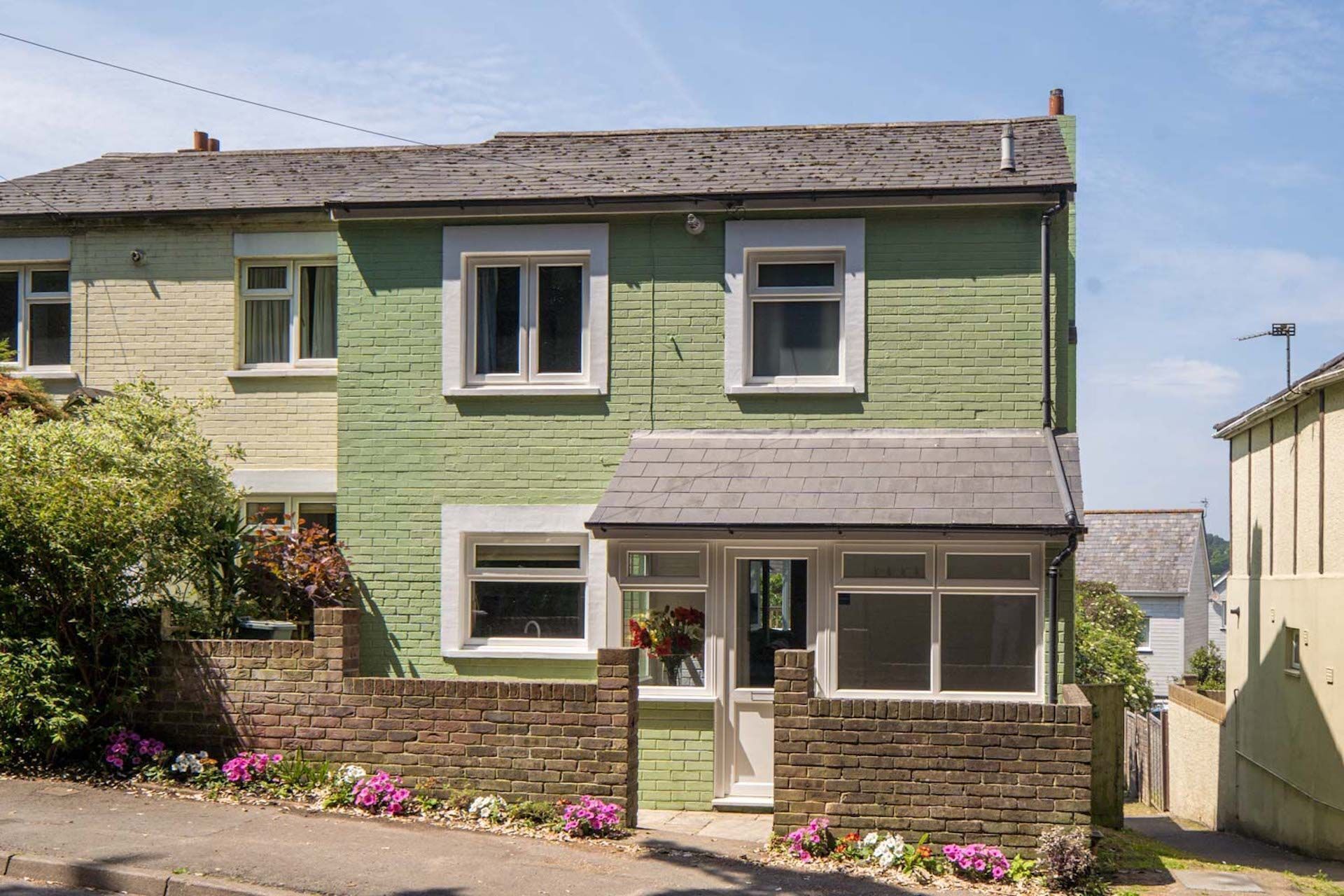 A two-story house with a green facade, white-framed windows, and a small front porch with a door.