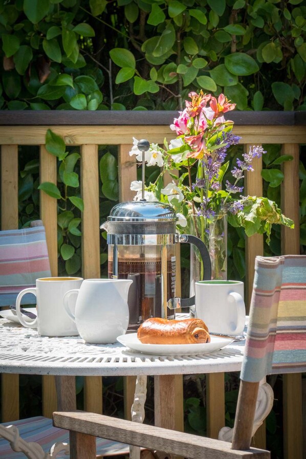Ett runt bord med en kaffebryggare, två vita koppar, en rulltårta och en vas med blommor.