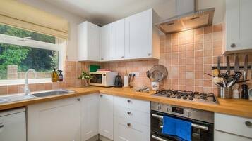 A modern kitchen with white cabinets, a wooden countertop, a gas stove, an oven, and a window with a view of greenery.