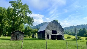 A rural landscape with a large barn, a smaller wooden structure, and a clear blue sky.