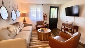A living room with a sofa, armchair, coffee table, and a TV mounted on the wall.