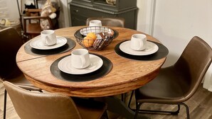 A round wooden dining table with four chairs, a central woven basket, and a cabinet in the background.