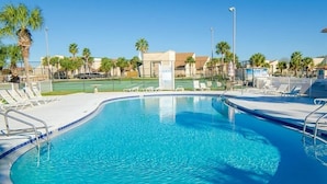 A clear blue swimming pool with lounge chairs and palm trees in the background.