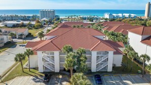 A coastal hotel with red-tiled roofs, a parking lot, and a view of the ocean.