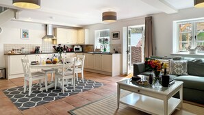Een moderne keuken met witte kastjes, een eethoek met een tafel en stoelen, en een woonkamer met een bank en salontafel.