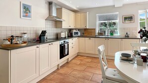 Een moderne keuken met witte kastjes, een inbouwoven, een magnetron en een raam met uitzicht op groen.