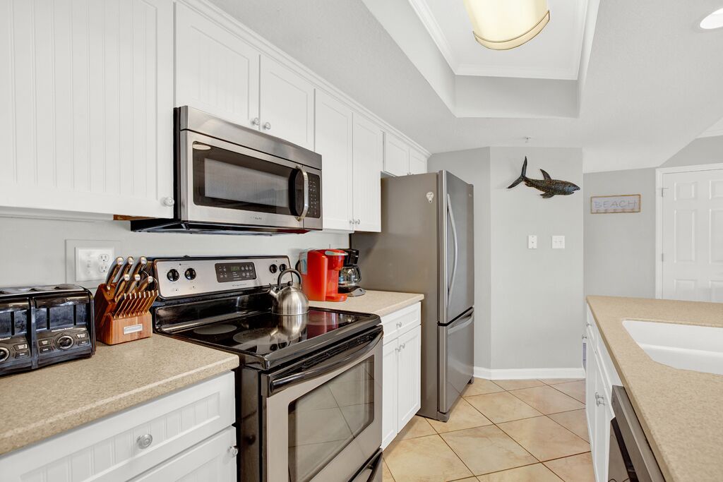 A modern kitchen with white cabinets, stainless steel appliances, and a tiled floor.