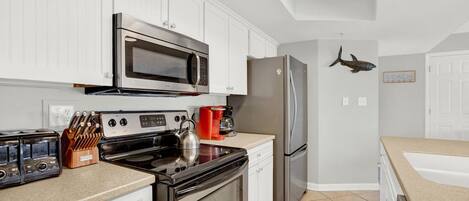 A modern kitchen with white cabinets, stainless steel appliances, and a tiled floor.