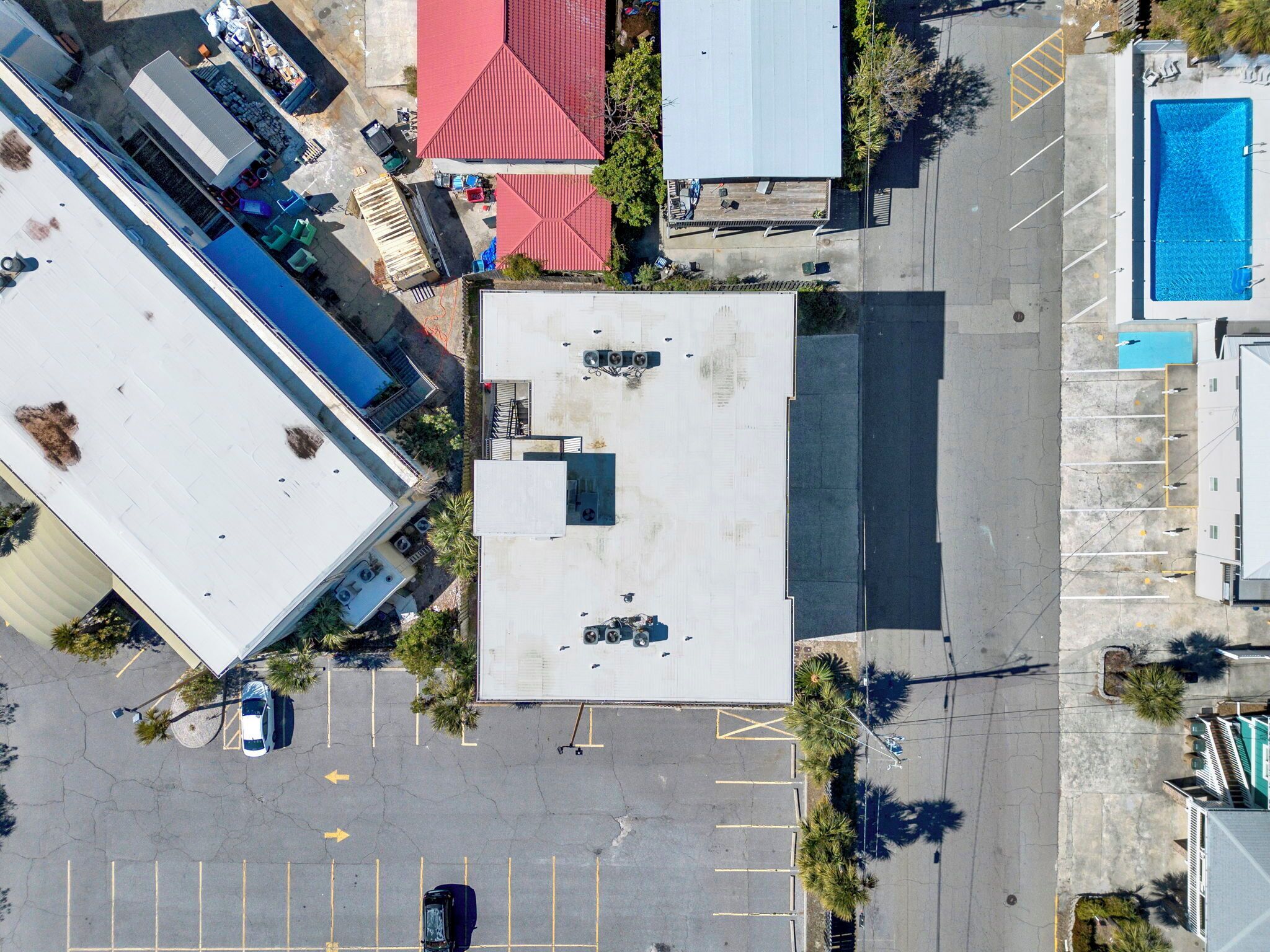 An aerial view of a parking lot with a building, a swimming pool, and a red-roofed structure.