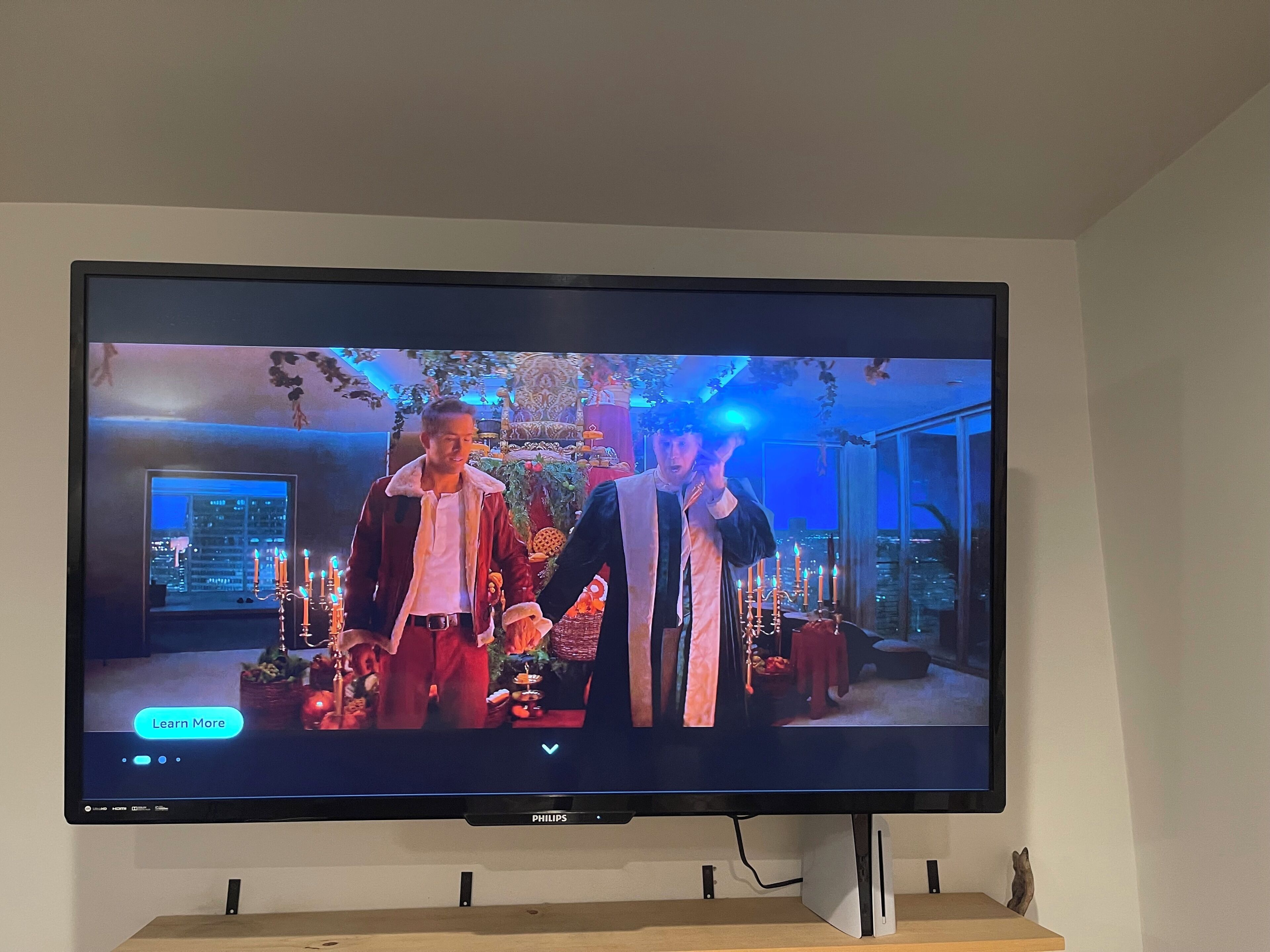 Een flatscreen-tv aan de muur met een scène van twee personen in een kamer met uitzicht op een stadsgezicht.