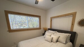 Un dormitorio con cama, dos ventanas, una mesita de noche y un adorno en la pared.