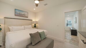 A bedroom with a bed, bedside lamps, a ceiling fan, and a painting on the wall. - A Wave From It All - Beach Cottage with Private Pool & Outdoor Area (Miramar Beach)