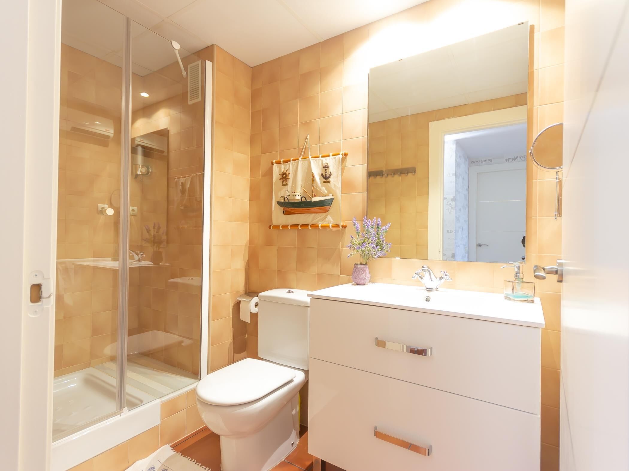 A bathroom with a glass shower enclosure, a toilet, a sink with a mirror, and a decorative towel rack.