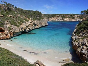 Un paysage côtier caractérisé par une eau turquoise cristalline, des falaises rocheuses et une plage de sable.